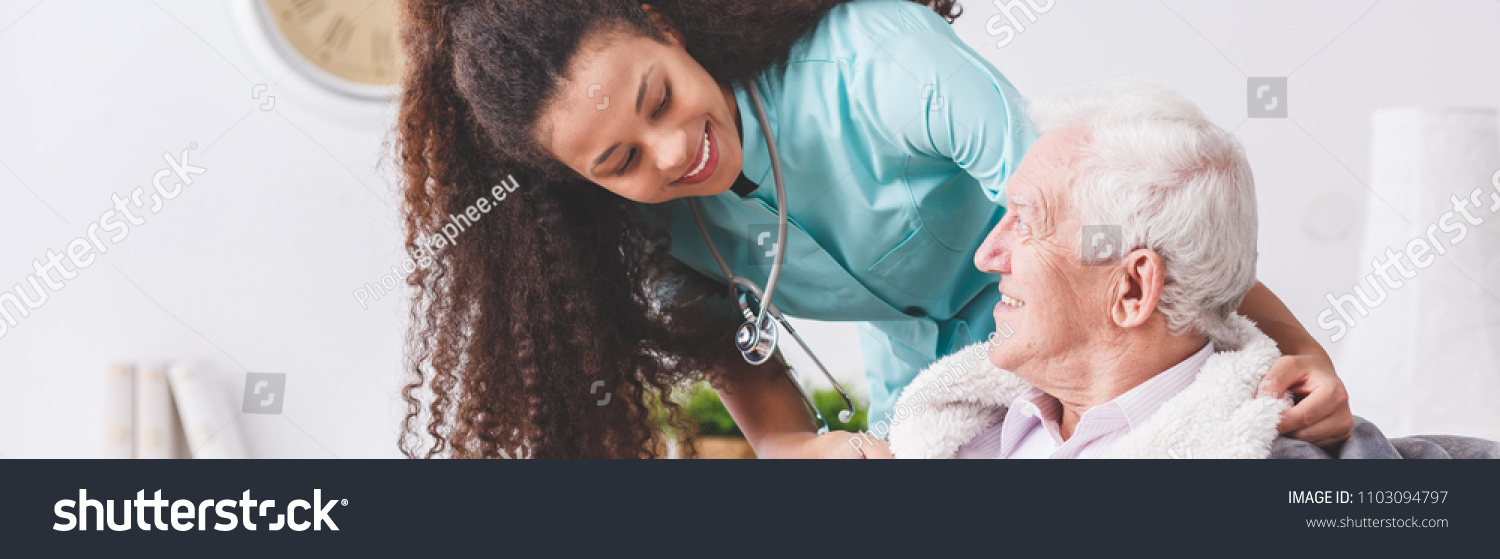 stock photo panorama of a happy nurse with a stethoscope covering an elderly man with a blanket in a nursing 1103094797